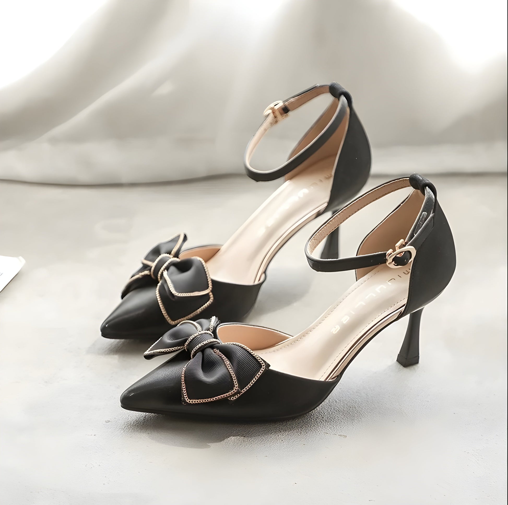 Elegant black women's high heels with pointed toes, gold-trimmed bow detail, and ankle strap design."